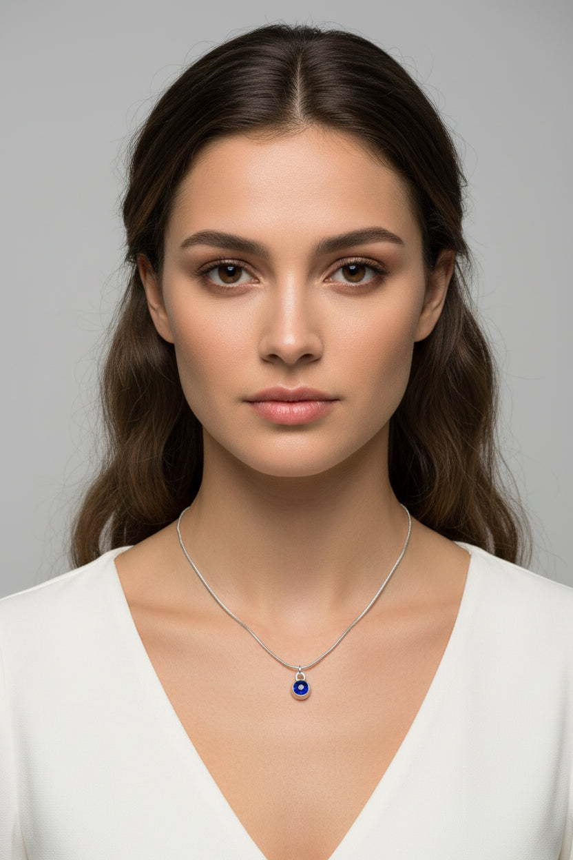 Woman in a white top wearing a silver snake chain necklace with September Sapphire birthstone pendant