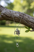 A silver-toned chain necklace with a dangling charm shaped like a stylized horseshoe and four leaf clover, displayed hanging over a branch.