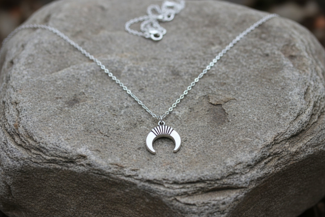 A silver crescent moon pendant necklace displayed on a large grey stone.