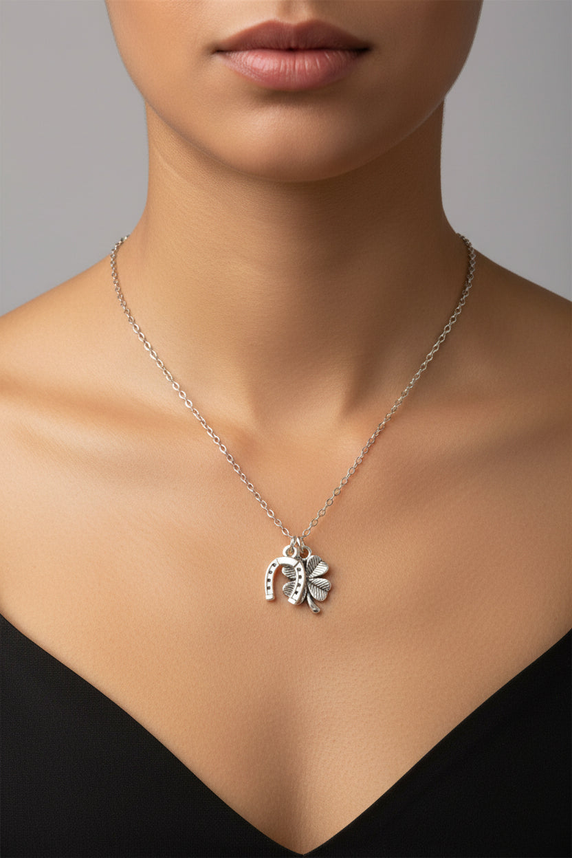 A silver-toned necklace with a small charm featuring a horseshoe and a four leaf clover, displayed on a white model.