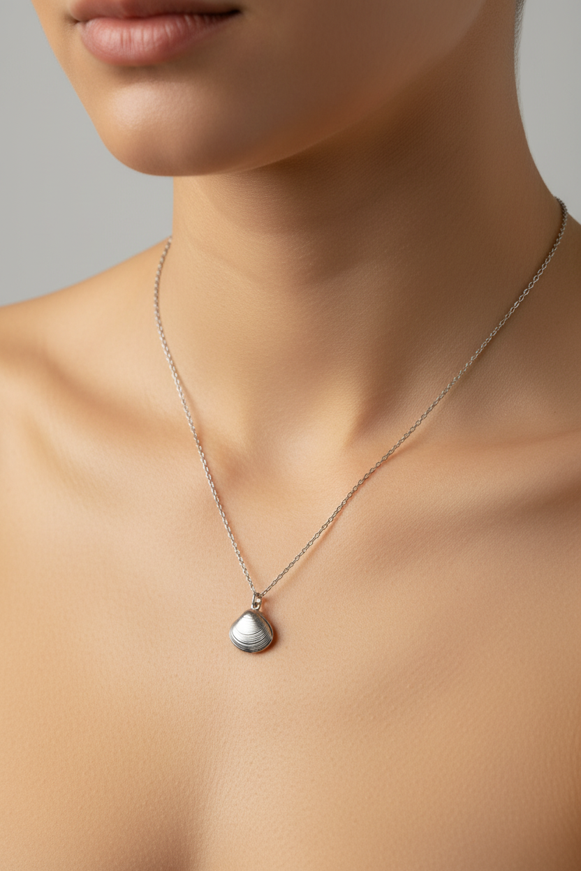 A close-up of a model's neck and upper chest wearing a delicate silver chain necklace with a small seashell silver pendant.