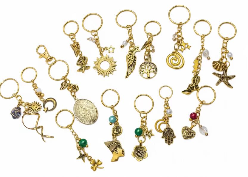 A set of 20 gold-toned keyrings with various charms, including stars, suns, hearts, flowers, and sea-themed motifs, arranged on a plain white background.