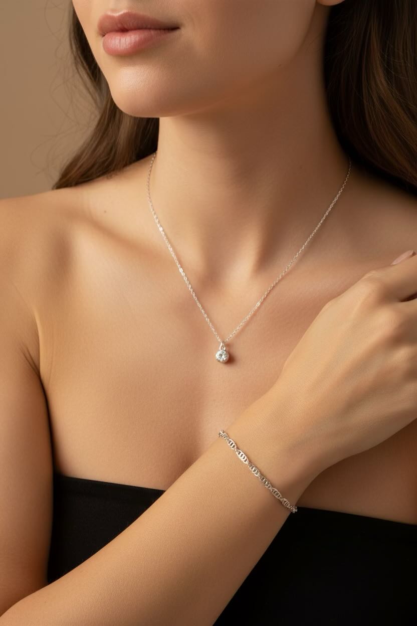 A close-up lifestyle shot of a model wearing a delicate silver necklace with a diamond April birthstone pendant and a silver water wave bracelet.