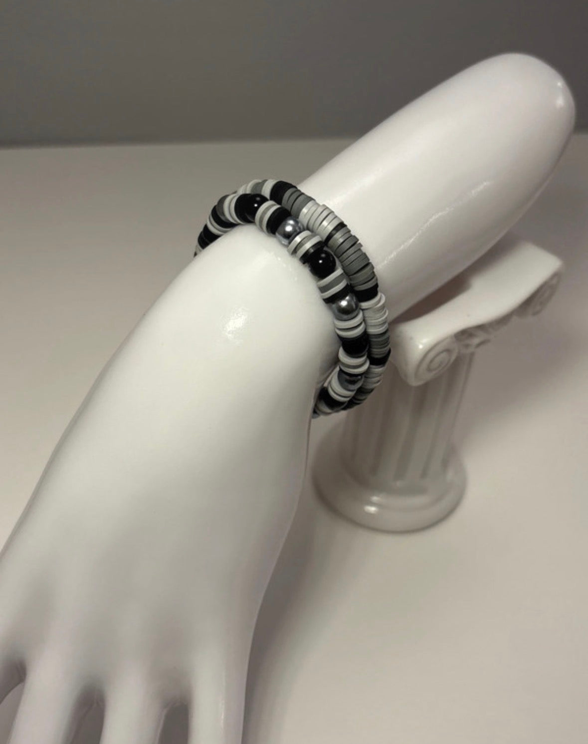 Black and gray beaded bracelet on a white mannequin hand against a gray background