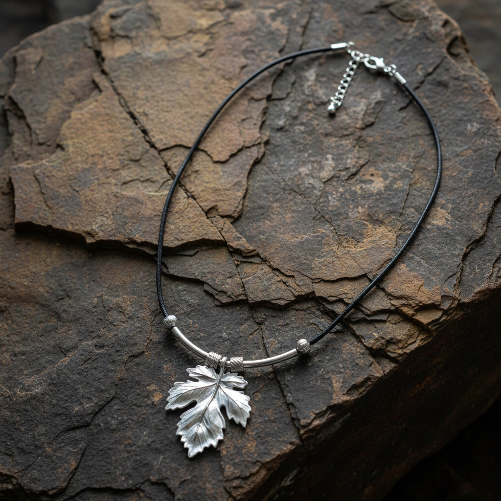 A silver-toned necklace with a textured leaf pendant, shown on a brown stone