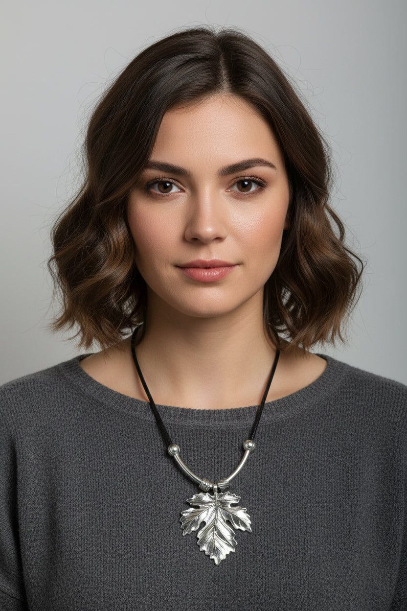 A silver leaf pendant necklace on a black cord, displayed on a model
