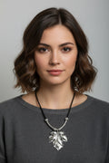 A silver leaf pendant necklace on a black cord, displayed on a model