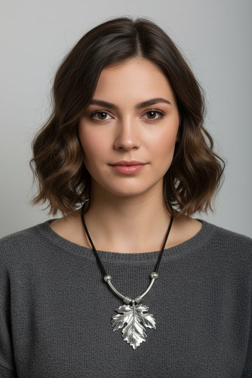 A silver leaf pendant necklace on a black cord, displayed on a model