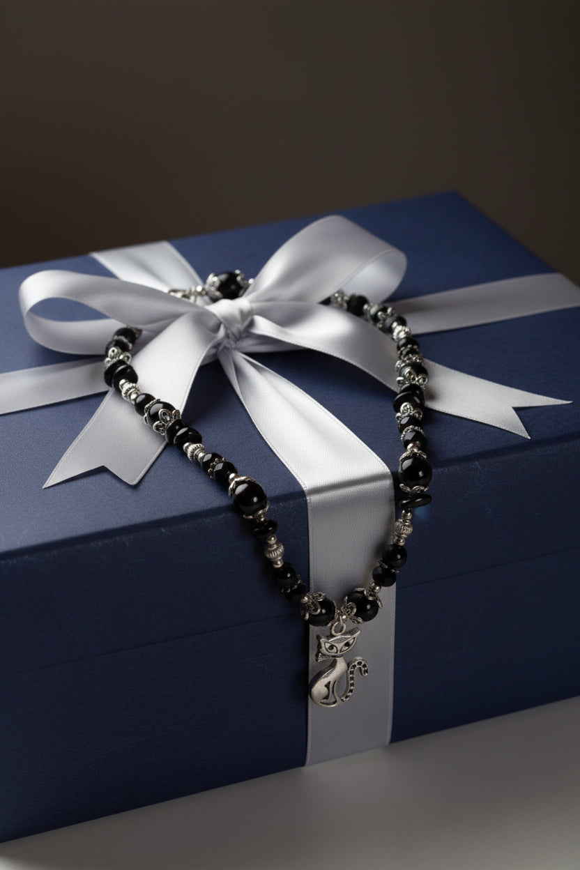 Necklace with black beads and a silver cat pendant on a large gift box