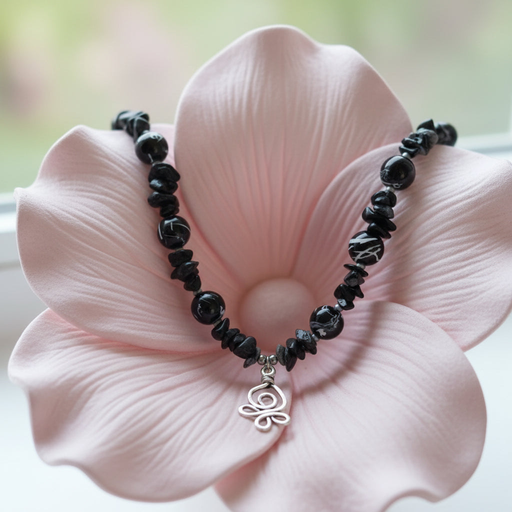 Black beaded bracelet with a silver flower pendant on a pink flower