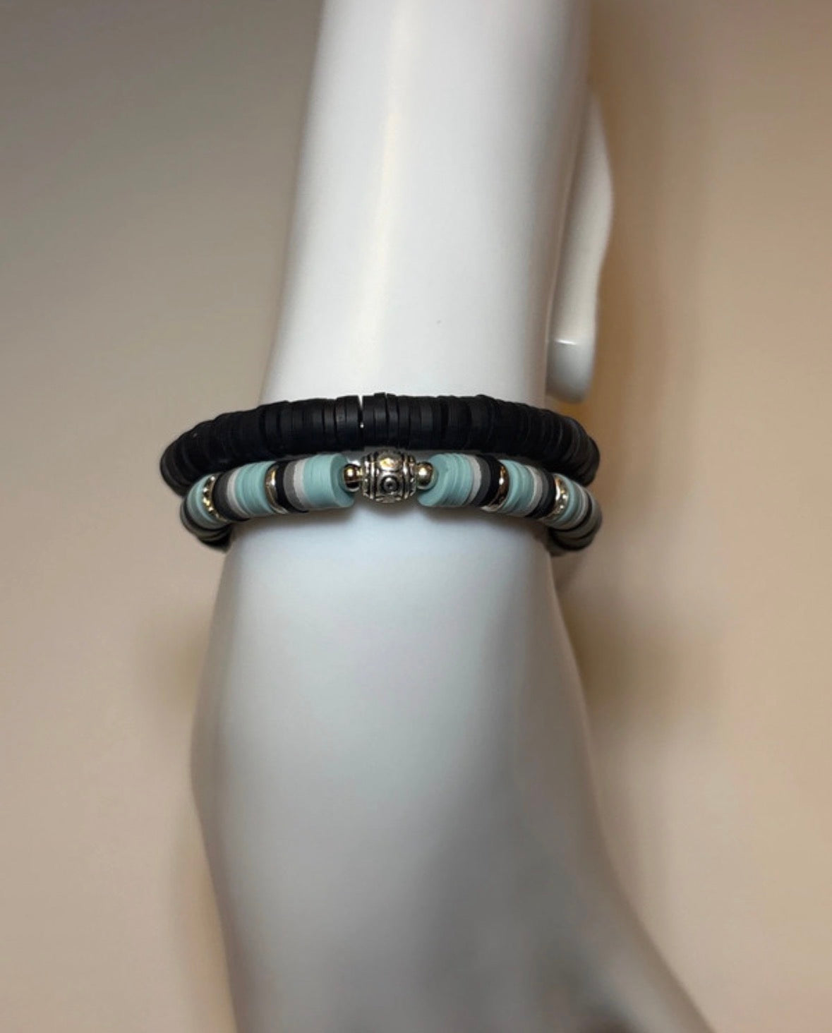 Bracelet with black and light blue beads on a mannequin arm against a beige background