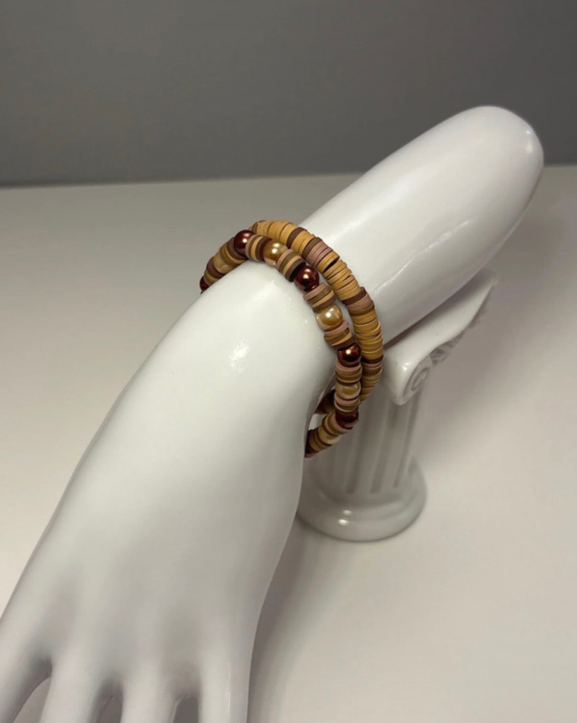 Brown/dark beige beaded bracelet on a white mannequin hand against a gray background