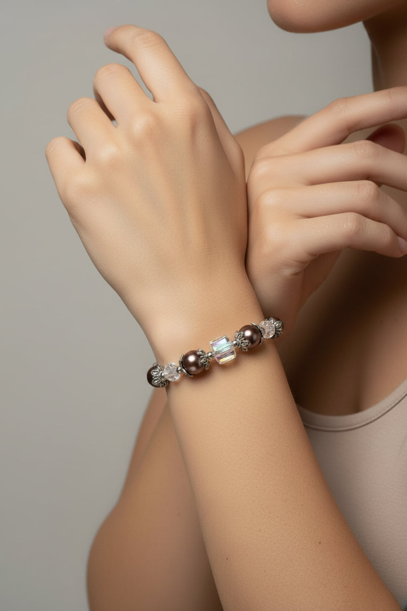 A beaded bracelet featuring dark brown glass pearls, silver filigree spacer beads, and clear faceted crystal beads, arranged in a circle on a light beige background.