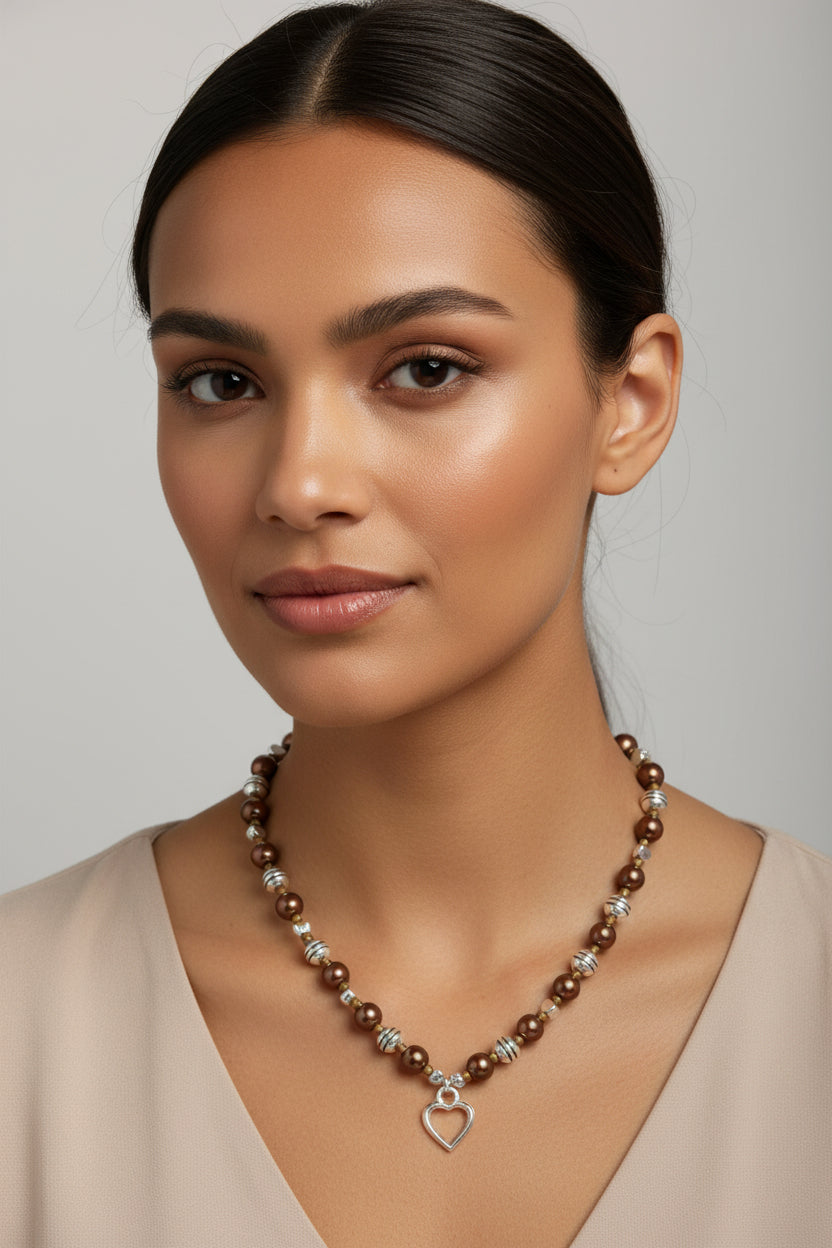 Woman wearing a brown beaded necklace with a heart pendant against a neutral background