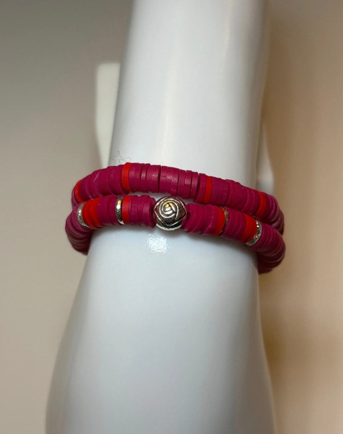 Red clay beaded bracelets on a white mannequin arm against a beige background