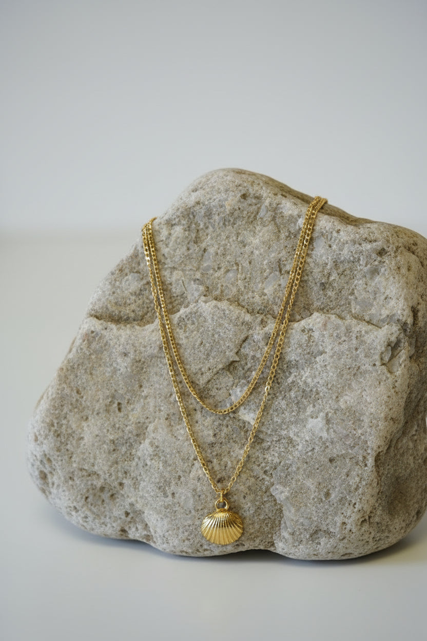 Gold double layered necklace with a small shell-shaped pendant on a large stone.