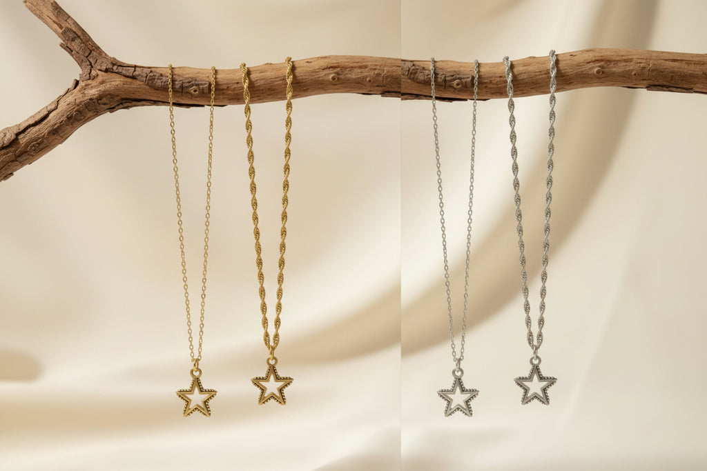 Two pairs of dangling star pendant necklaces hanging from a rustic branch against a soft cream fabric backdrop. One pair is gold-toned and the other is silver-toned.