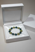 A beaded bracelet with dark teal and sage green pearls, displayed inside an open white jewelry box.