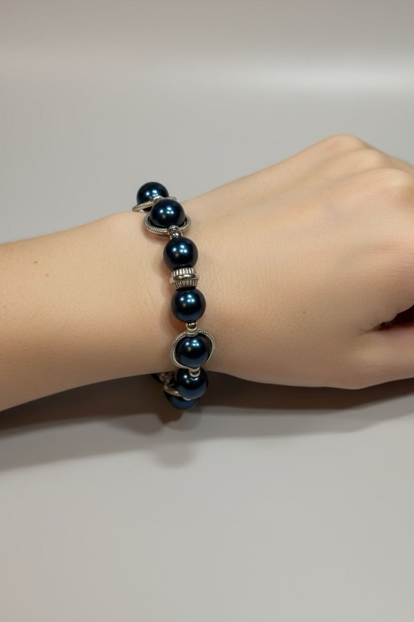 A steel blue pearl bracelet with silver spacer beads worn on a person's wrist, shown against a neutral gray background.