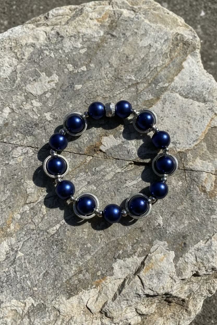 A beaded stretch bracelet with dark royal blue glass pearls and silver-toned spacer rings, displayed on a textured gray stone surface.