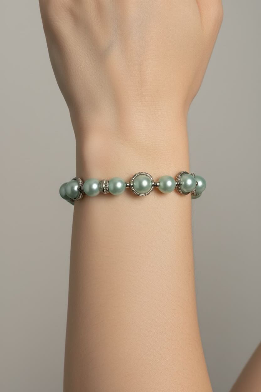 A close-up of a person's wrist wearing a bracelet made of aqua blue pearls and silver-toned metal links.