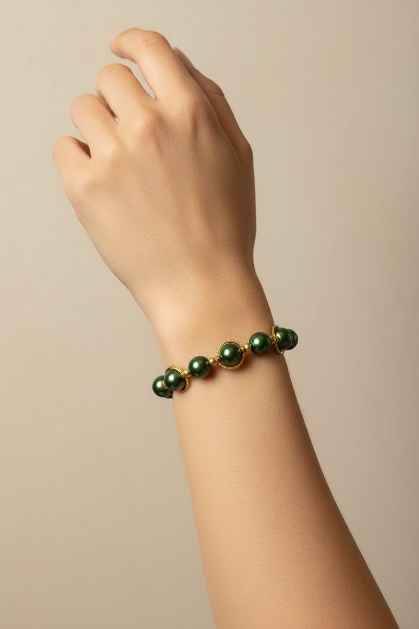 A close-up of a person's wrist wearing a bracelet made of dark green glossy pearls with small gold spacer rings, set against a plain beige background.