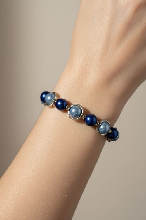 A close-up of a person's wrist wearing a beaded bracelet with dark royal blue and aqua blue pearls separated by small silver-toned spacer beads.