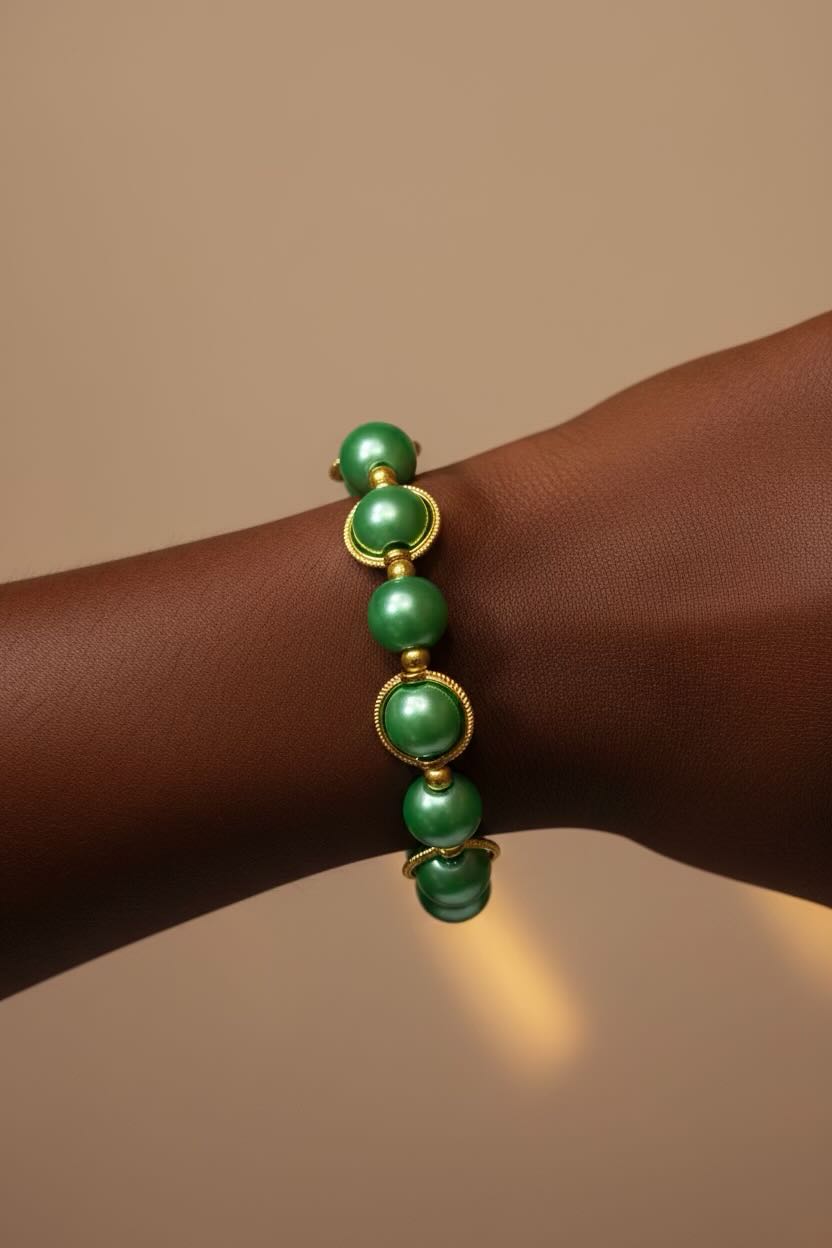 A close-up of a sea green glass pearl bracelet with gold-toned circular accents worn on a person's wrist against a warm beige background.