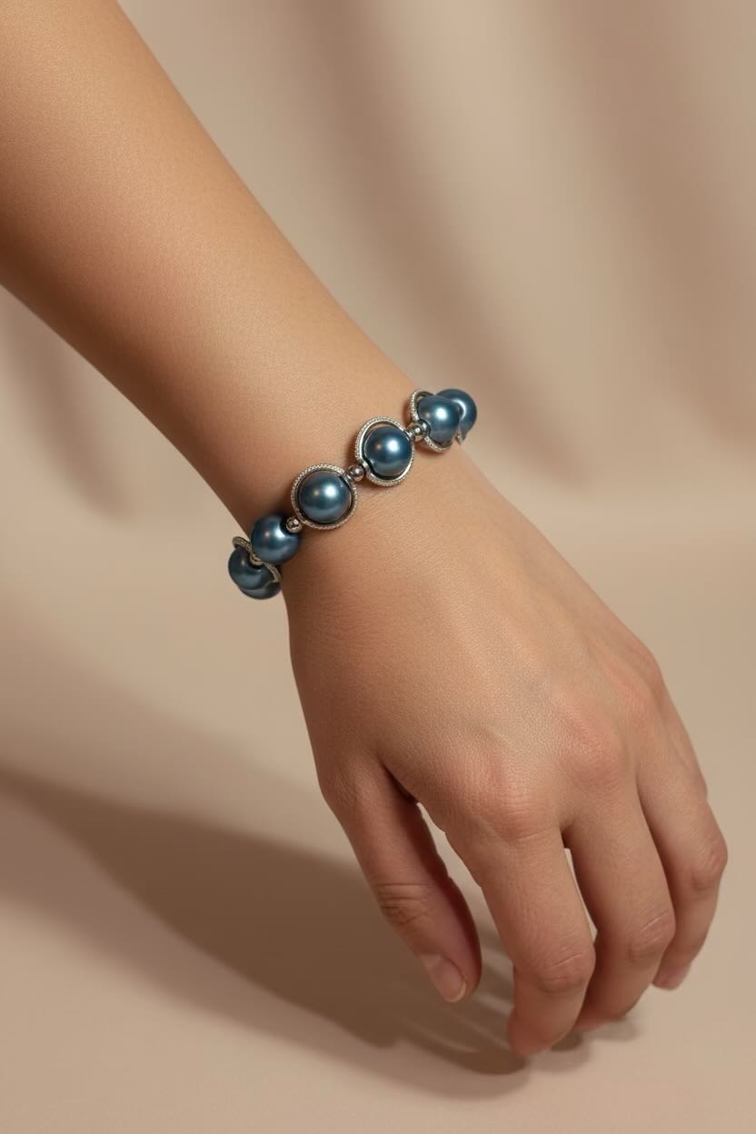 A close-up of a person's hand and wrist wearing a bracelet made of teal blue round pearls set in silver-toned metal, against a warm beige background.