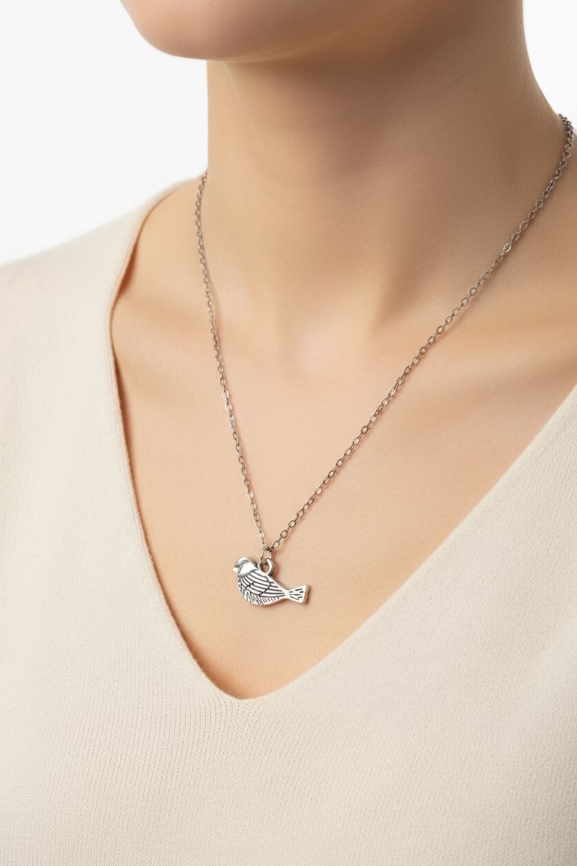 Necklace with a bird pendant worn by a person in a beige sweater