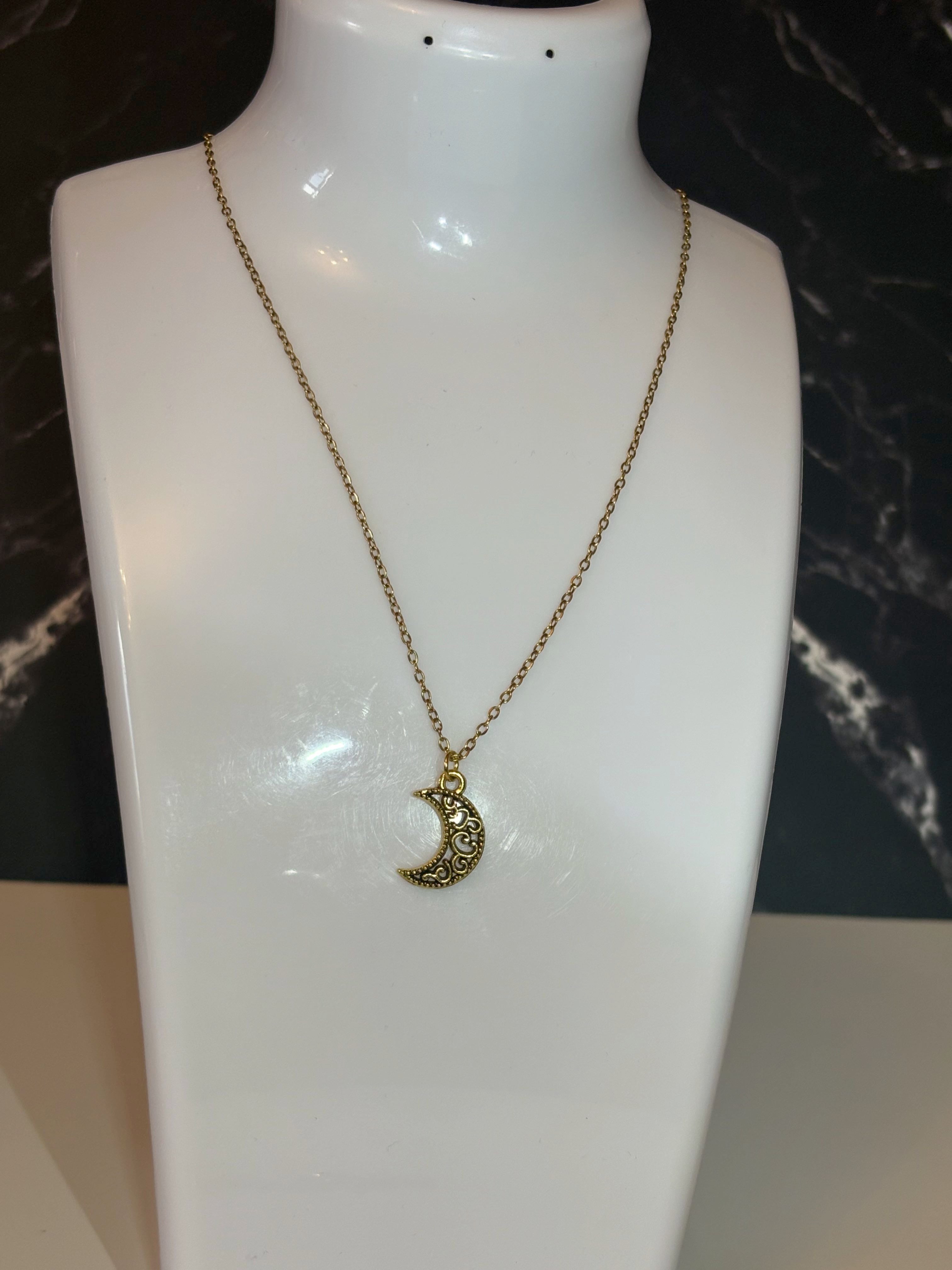 A gold crescent moon pendant necklace displayed on a white mannequin bust against a dark marble-patterned background.