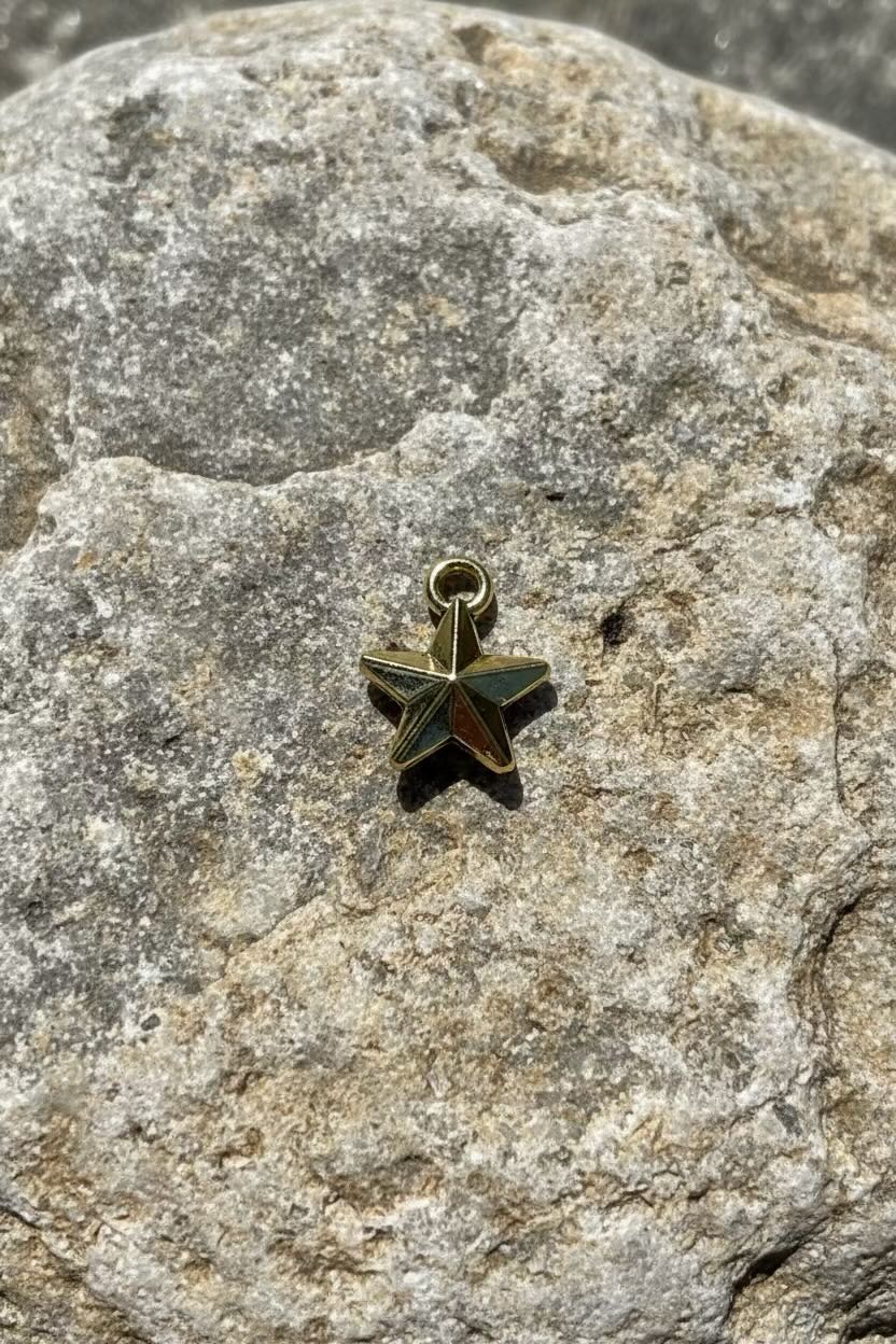 A small gold 3D star-shaped charm with a top loop, resting on a textured gray stone surface.