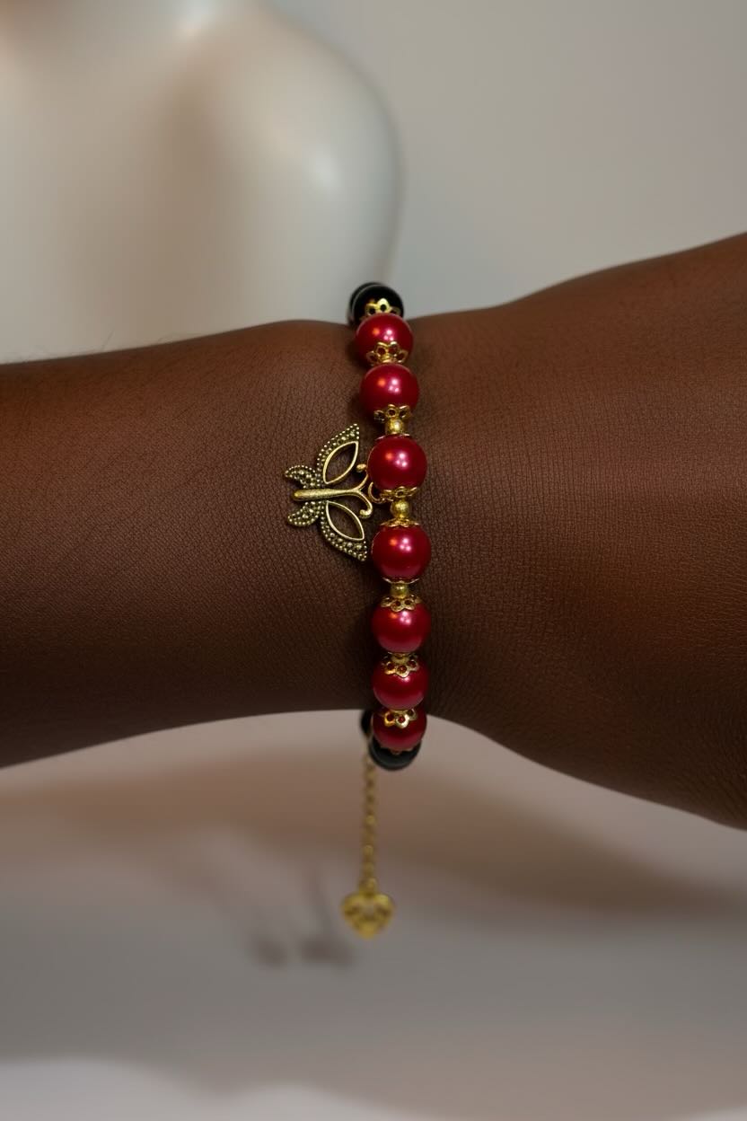 A close-up of a beaded bracelet worn on a person's wrist. The bracelet features glossy red and black pearls, small gold spacer beads, a gold butterfly charm, and black accent beads, with a small gold dangling charm at the end.