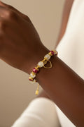 A close-up of a person's wrist wearing a delicate gold bracelet with white and red glass pearls, and a small gold heart charm.
