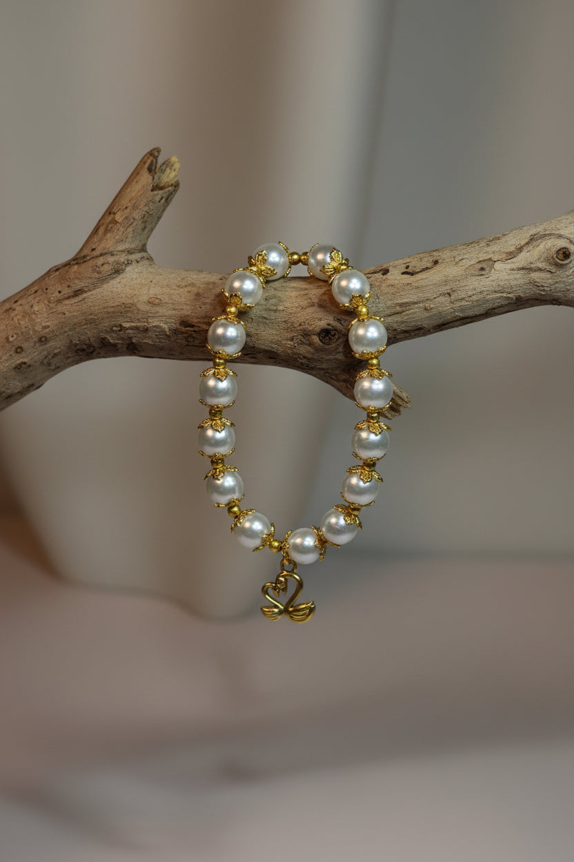 A gold and white beaded bracelet with pearl-like beads and small gold charms, displayed hanging from a branch.