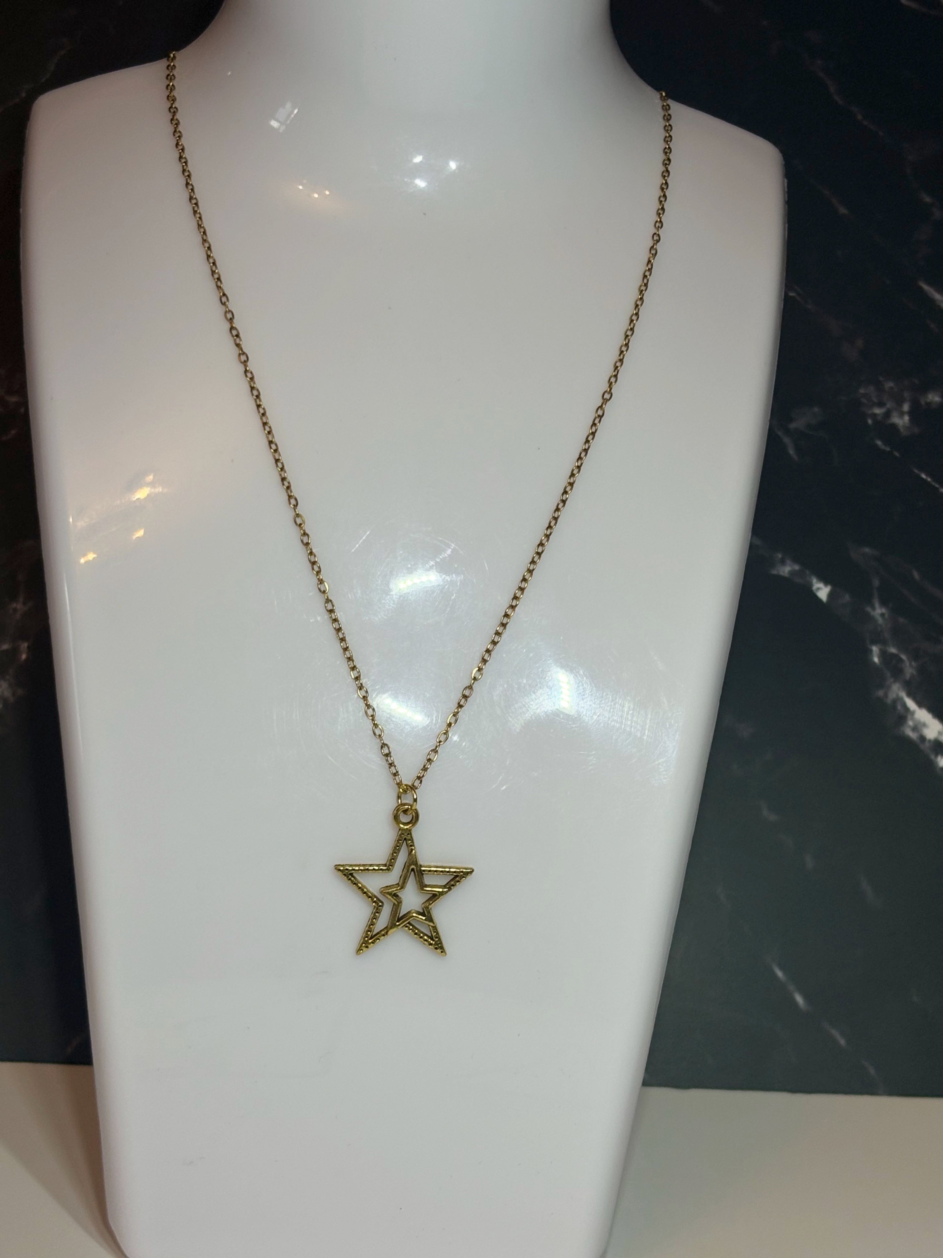 A gold-toned star pendant necklace displayed on a white jewelry bust against a dark marble-patterned background.