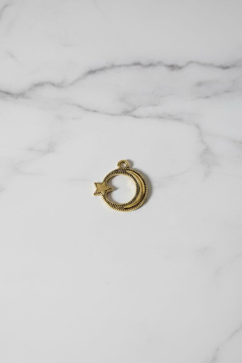 A small gold crescent moon and star charm with a textured finish, resting on a white marble surface.