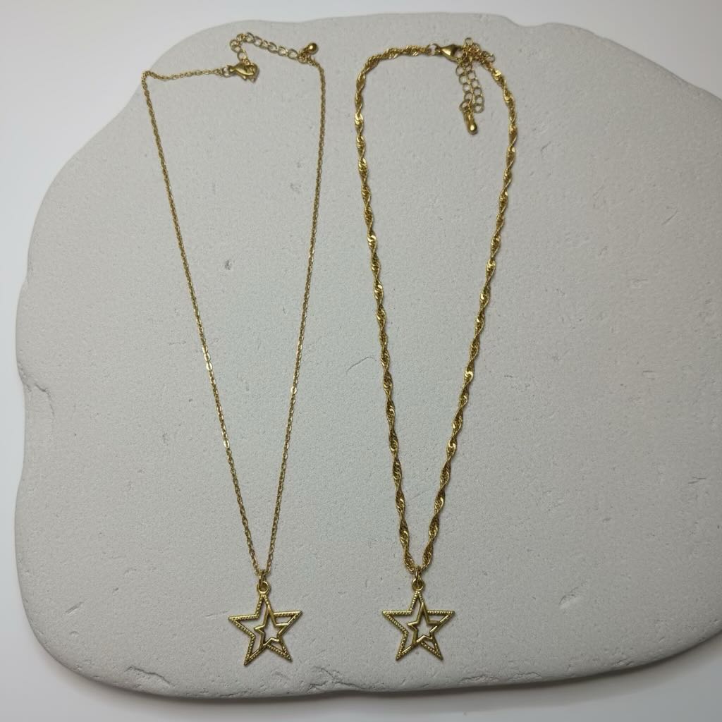 Two gold star pendant necklaces displayed on a light gray stone slab against a white background.