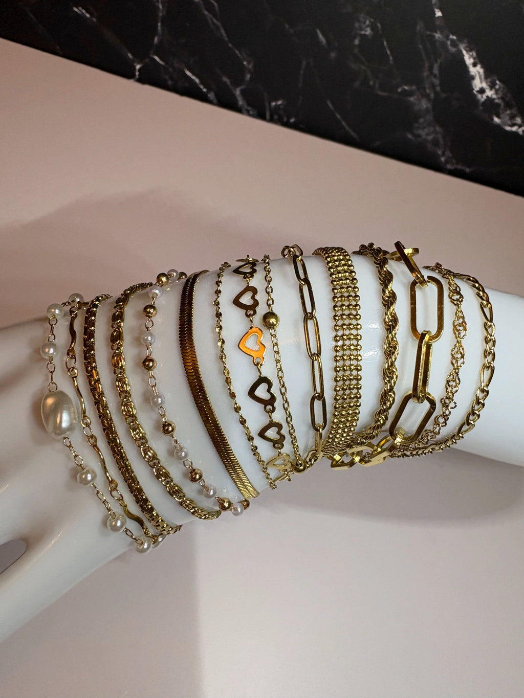 A collection of gold and silver chain bracelets with heart charms and pearl accents, displayed on a white mannequin arm.