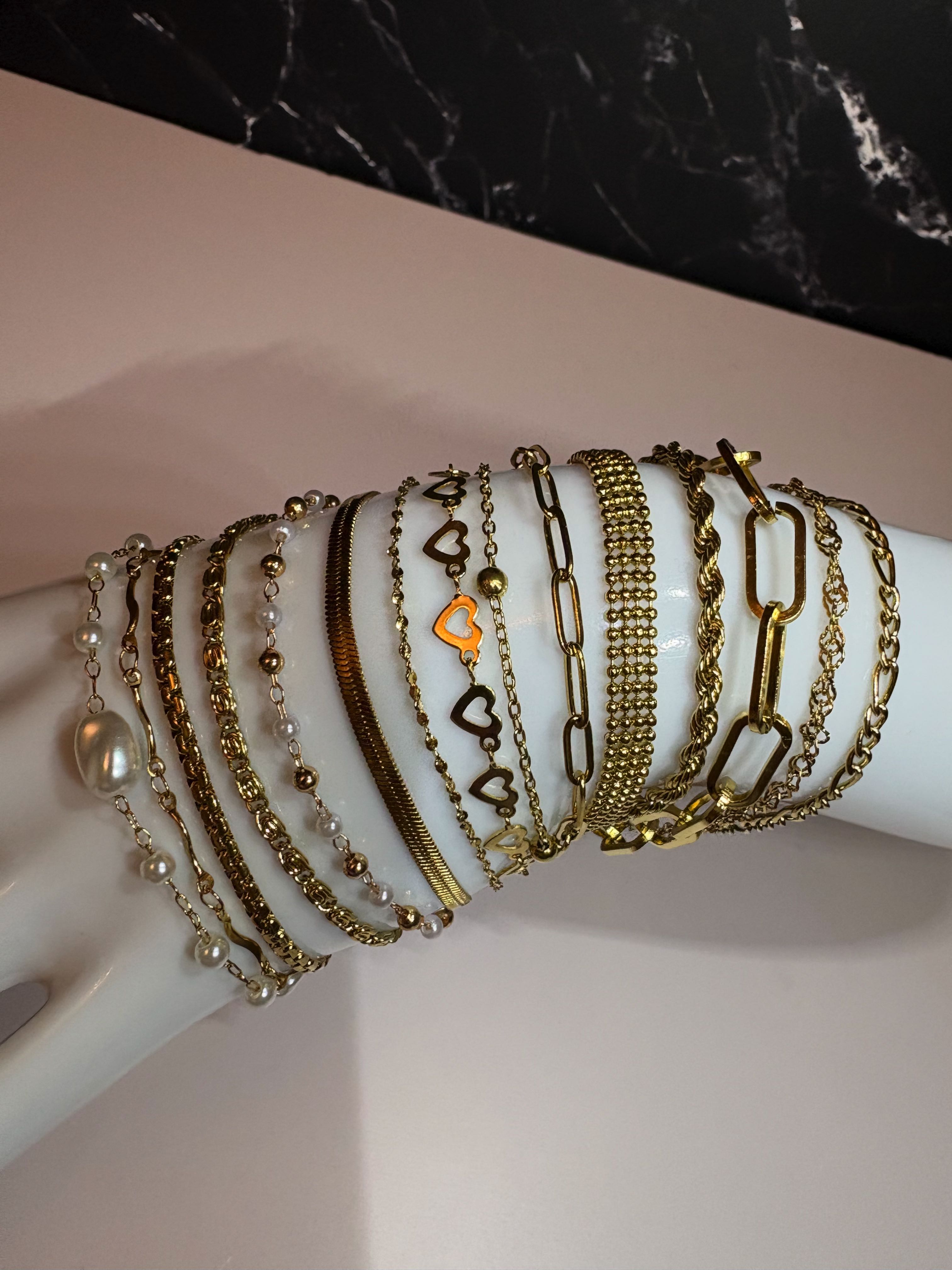 A collection of gold and silver chain bracelets with heart charms and pearl accents, displayed on a white mannequin arm.