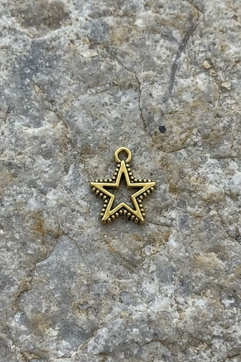 A small gold-toned star-shaped charm with a decorative loop at the top, placed on a textured gray stone surface.