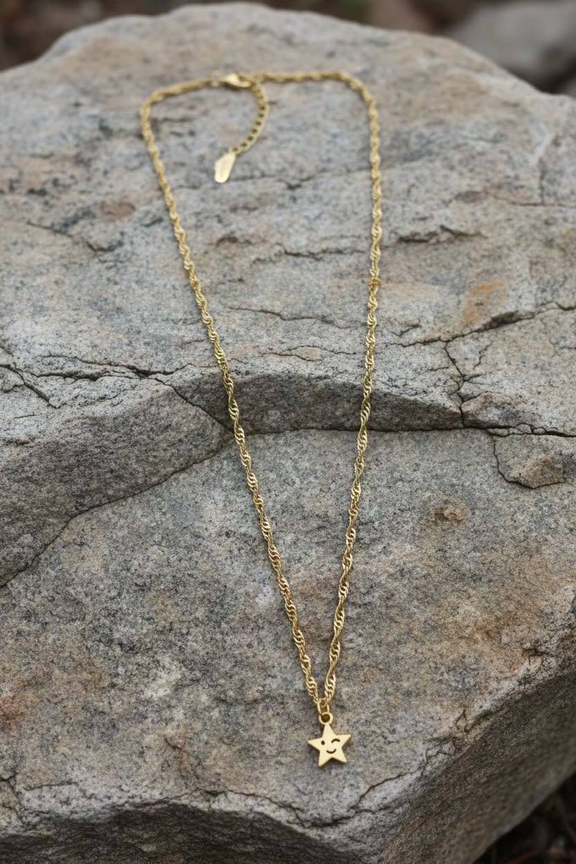 A delicate gold chain necklace with a small star-shaped pendant resting on a textured gray rock.