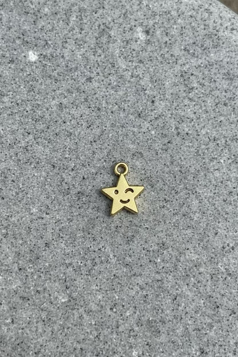 A small gold star charm with a simple smiley face, resting on a textured gray stone surface.