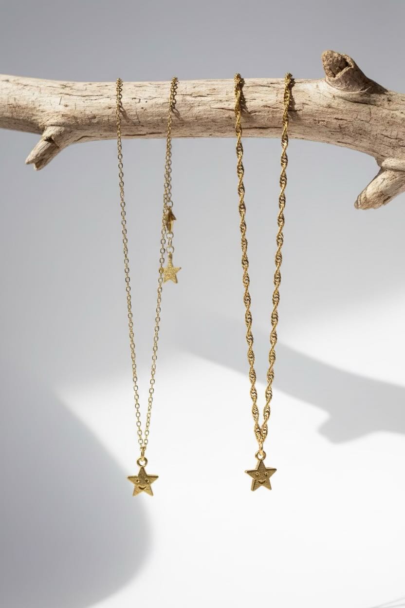 Two gold star pendant necklaces hanging from a natural driftwood branch against a clean white background.