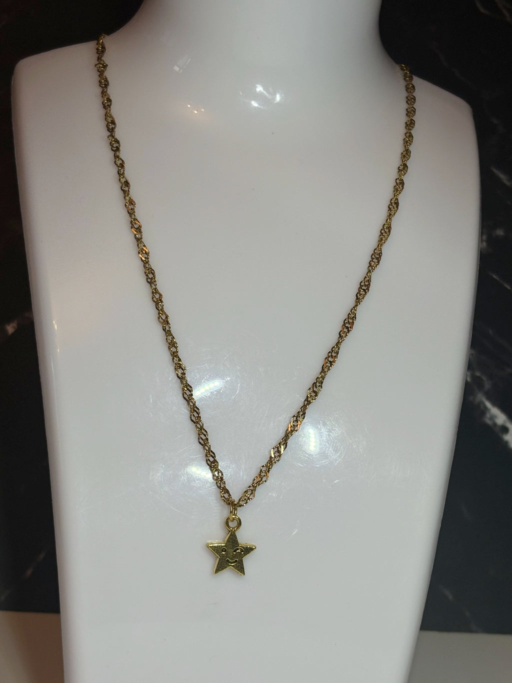 A gold-toned chain necklace with a small star-shaped pendant, displayed on a glossy white mannequin bust.