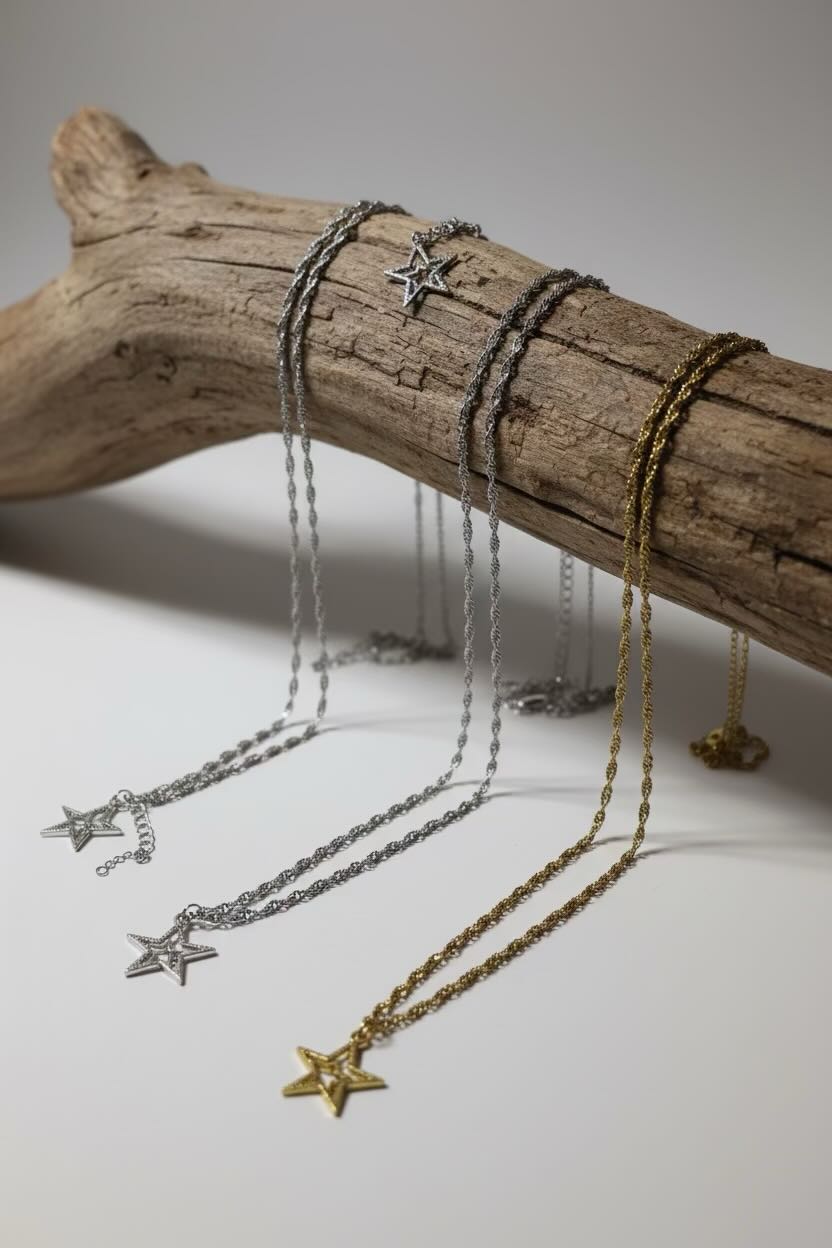 Three delicate star pendant necklaces in silver and gold tones draped over a rustic driftwood branch on a light gray background.