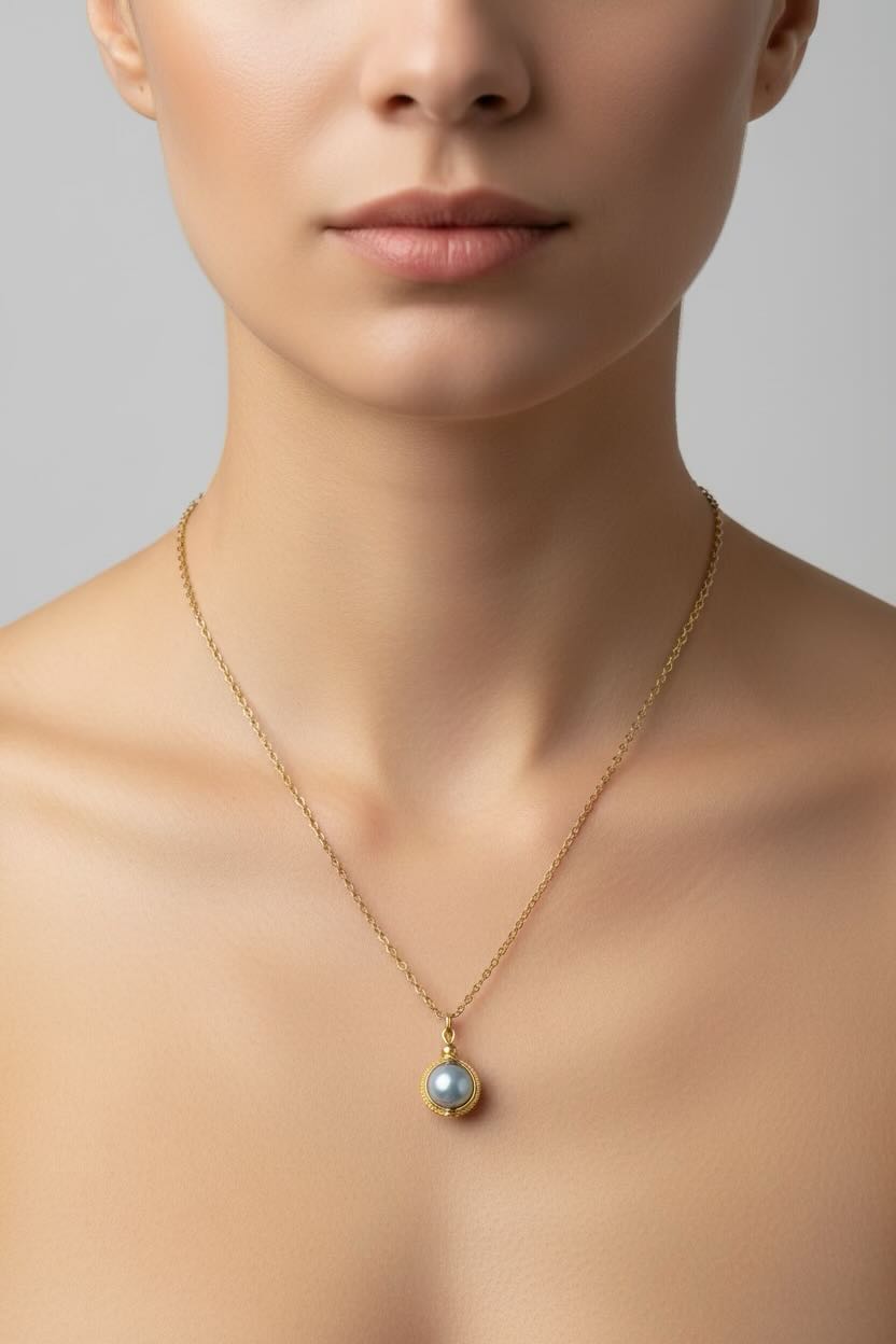 A close-up of a model wearing a delicate gold chain necklace with a small round iridescent baby blue pearl pendant.