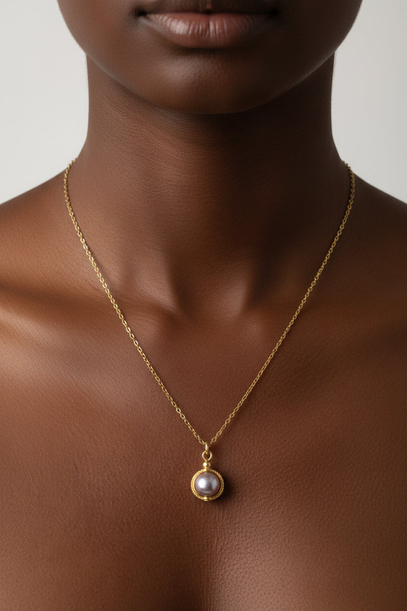 Gold cable chain necklace with round lavender glass pearl pendant in gold rope-edged setting on a model