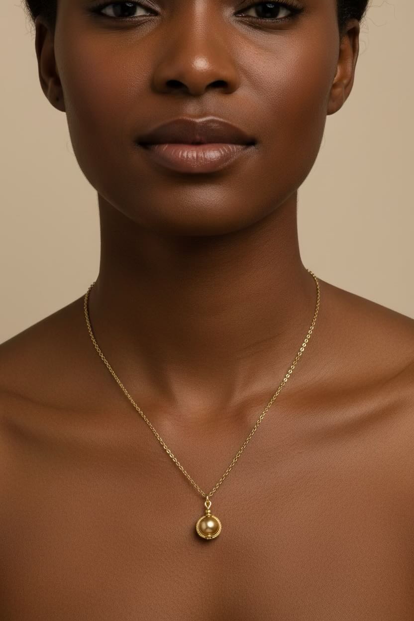 A gold chain necklace with a small oval pendant featuring a gold pearl set in a gold bezel, displayed on a model.