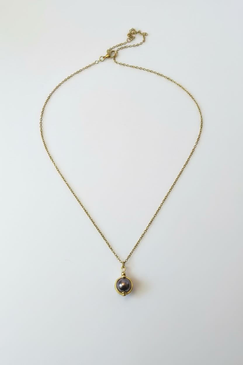 A delicate gold chain necklace with a small gold bezel holding a saddle brown round pearl pendant, displayed on a clean white background.